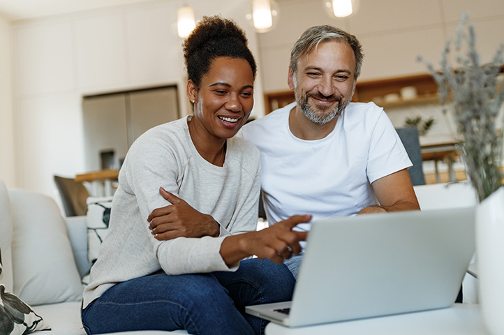 man and women sitting on the couch together smiling into their laptop computer